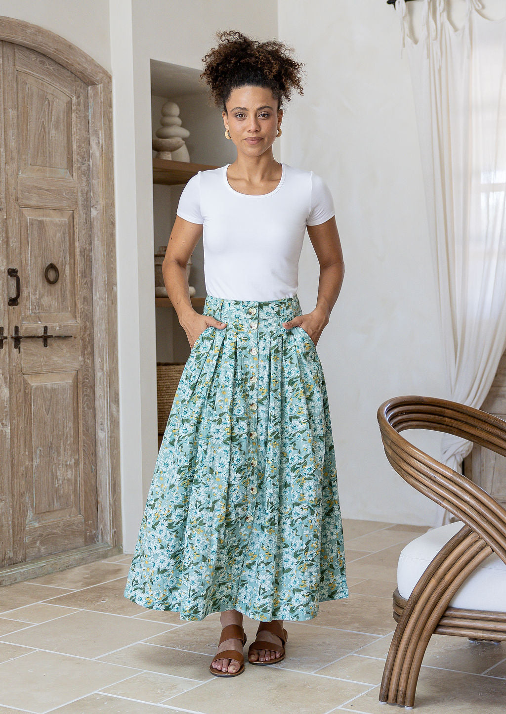 Woman wearing a white basic top and floral button through shin length cotton skirt with box pleats, belt loops and pockets.