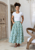 Woman wearing a white basic top and floral button through shin length cotton skirt with box pleats, belt loops and pockets.