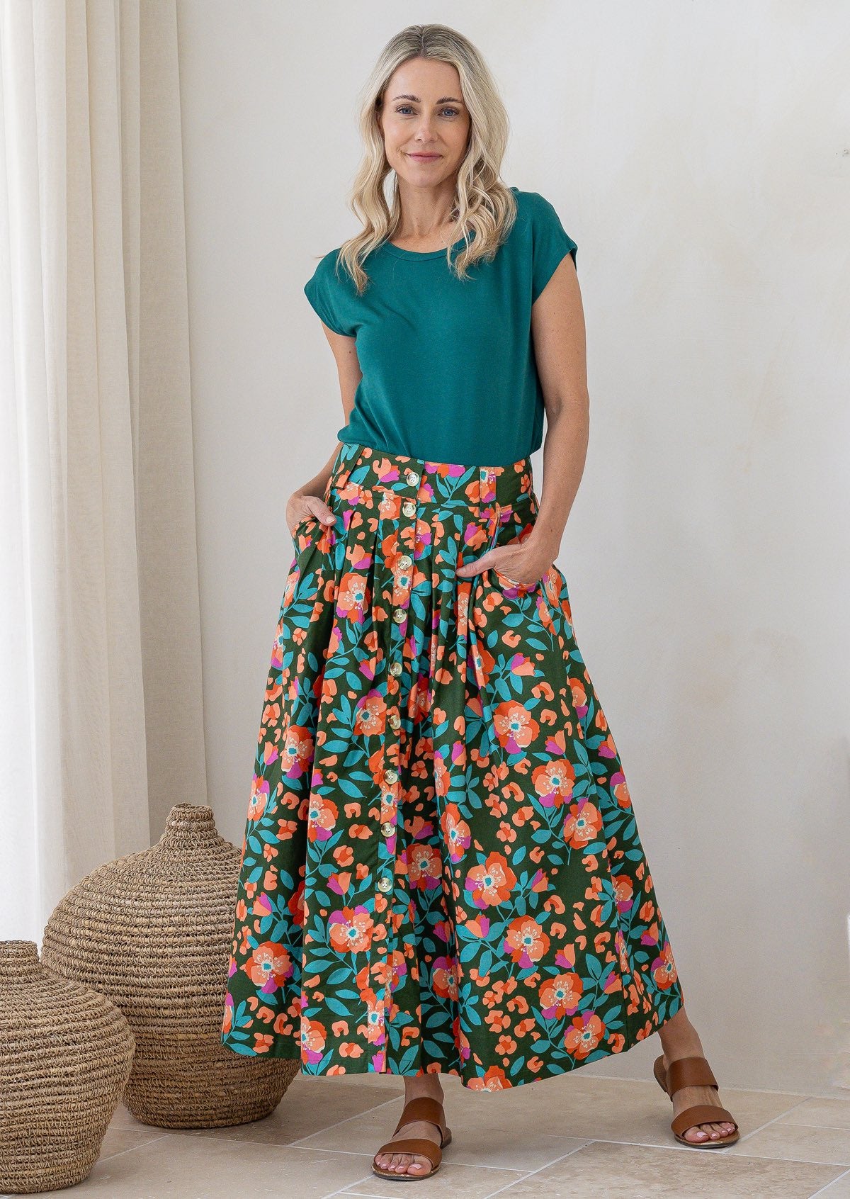 Woman standing with both hand in pockets wears 100% cotton button through skirt in olive green based floral print. 
