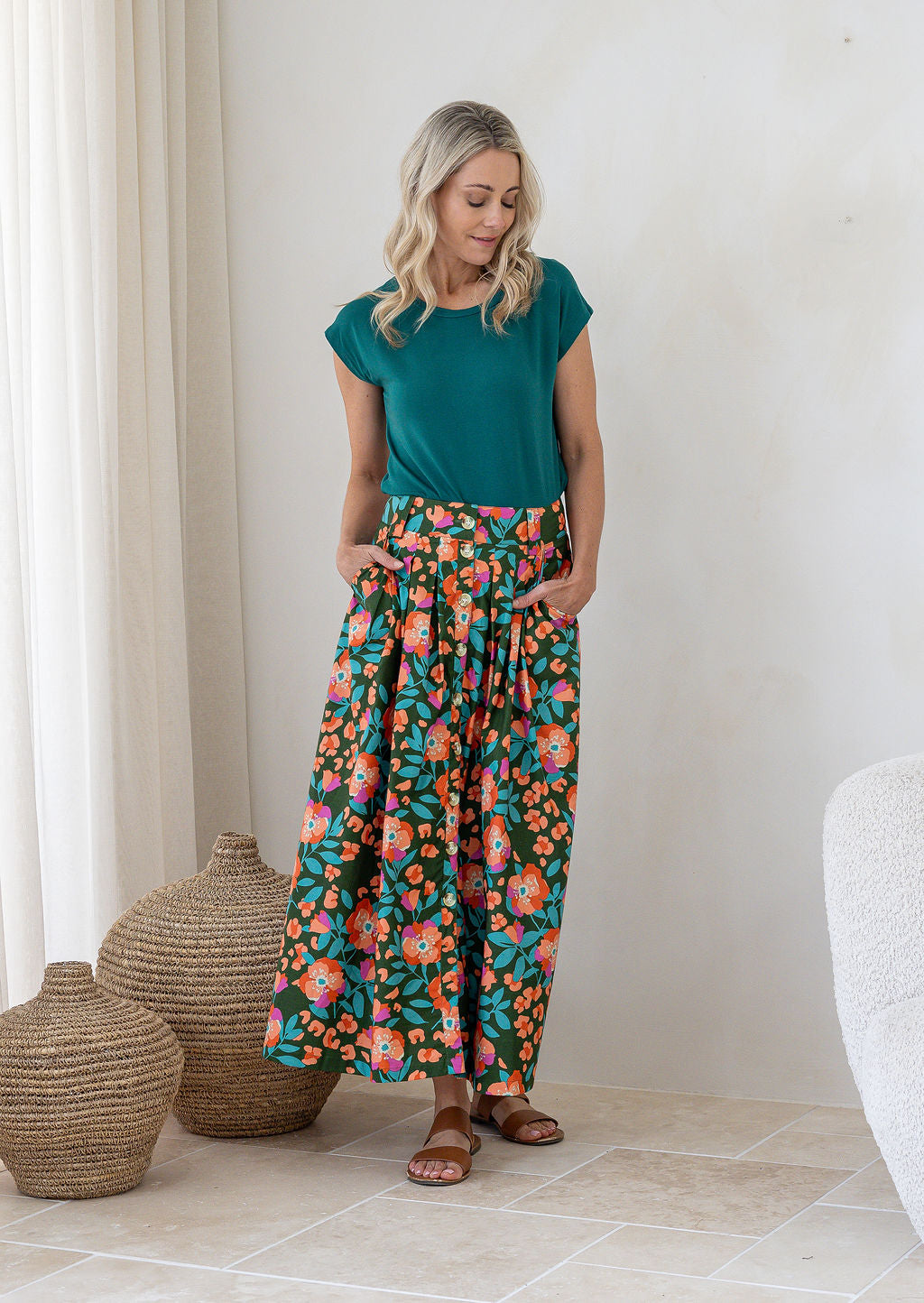 Woman wearing a basic top and floral button through shin length cotton skirt with box pleats, belt loops and pockets.