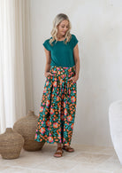 Woman wearing a basic top and floral button through shin length cotton skirt with box pleats, belt loops and pockets.