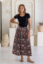 Woman wearing a black basic rayon top and floral button through shin length cotton skirt with box pleats, belt loops and pockets.