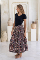 Woman poses in 100% cotton button through a-line skirt with box pleats, belt loops and pockets in black based traditional indian floral print 