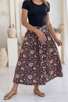 Close up image of a model wearing button through cotton skirt with box pleats and belt loops in black based indian floral print.