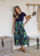 Woman wearing a navy basic top and floral peacock button through shin length cotton skirt with box pleats, belt loops and pockets.