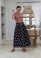 Woman wearing a basic top and floral button through shin length cotton skirt with box pleats, belt loops and pockets.