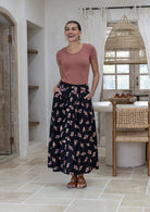 Woman stands wearing a basic top and floral print, shin length cotton skirt with button through front and box pleats.
