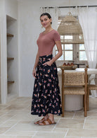 Woman stands sideways wearing a basic top and floral print, shin length cotton skirt with button through front and box pleats.