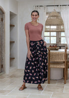Woman stands wearing a basic top and floral print, shin length cotton skirt with button through front and box pleats.