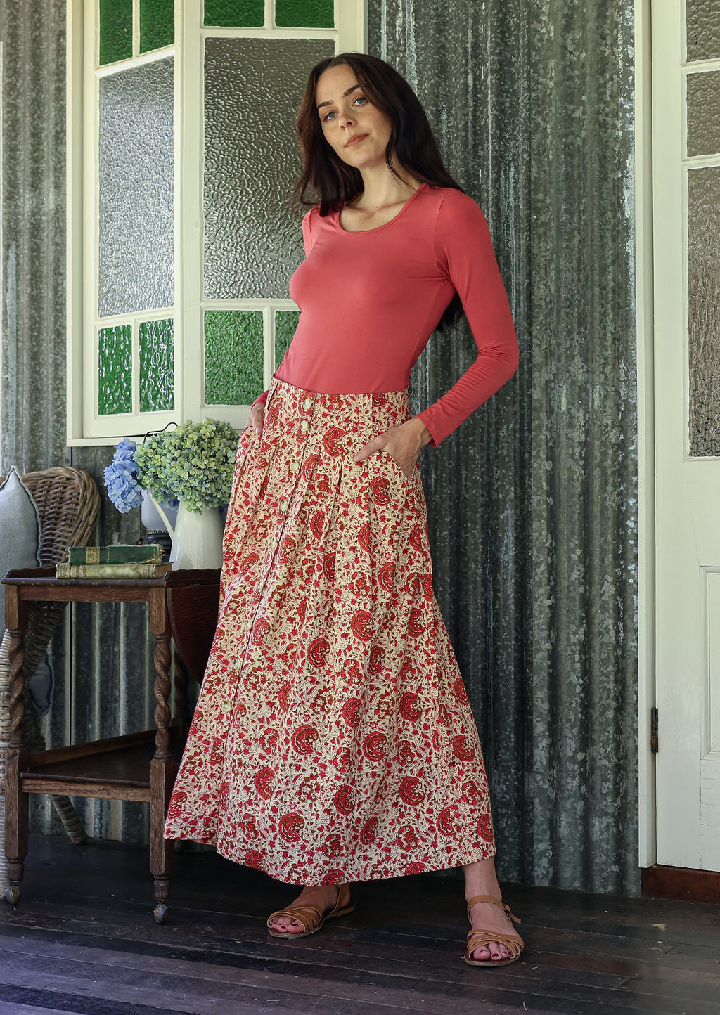 Woman wearing a pink basic top and floral button through shin length cotton skirt with box pleats, belt loops and pockets.