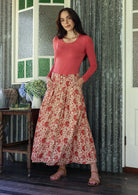 Woman standing with both hand in pockets wears 100% cotton button through skirt in gentle cream based floral print. 
