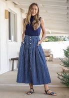 Woman standing with both hand in pockets wears 100% cotton button through skirt in navy based white striped print. 