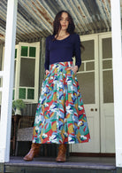 Woman wearing a colorful patterned skirt and navy top standing on a porch.