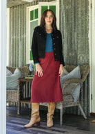 Woman in cotton corduroy red skirt and black jacket standing in a room with wicker furniture.