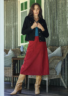 Woman wearing a black cotton corduroy jacket with brass buttons and pockets, [aired with a blue top, red skirt, and tan boots