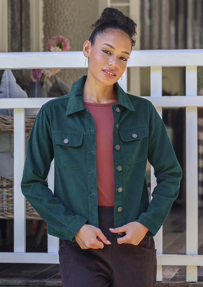 Woman wearing a jacket in deep, luxurious, deep blue green standing against a white railing