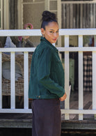 Woman stands sideways wearing a corduroy jacket and corduroy pants against a white railing.