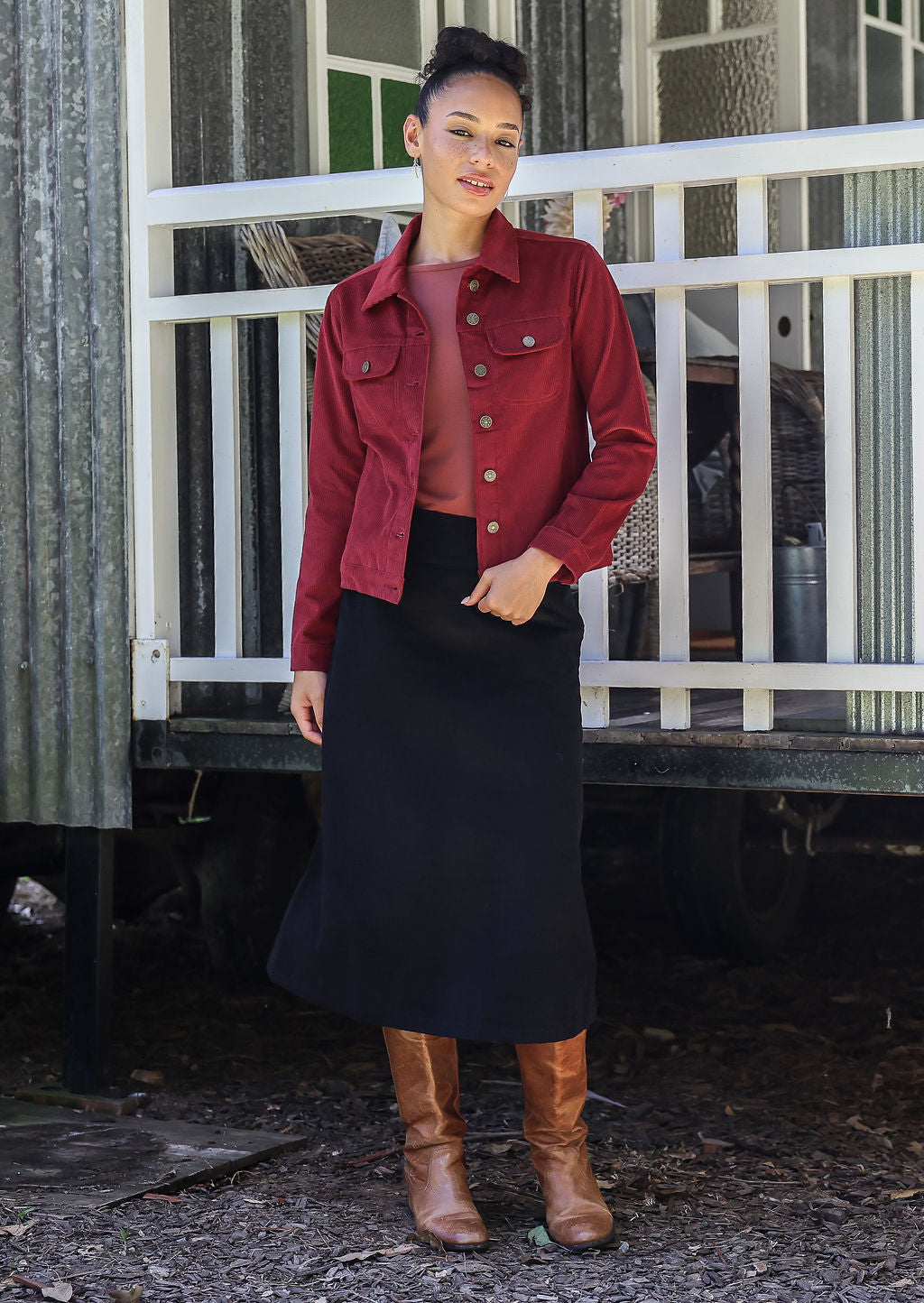 Woman wearing a jacket in deep, luxurious, and intense red-purple hue  standing against a white railing