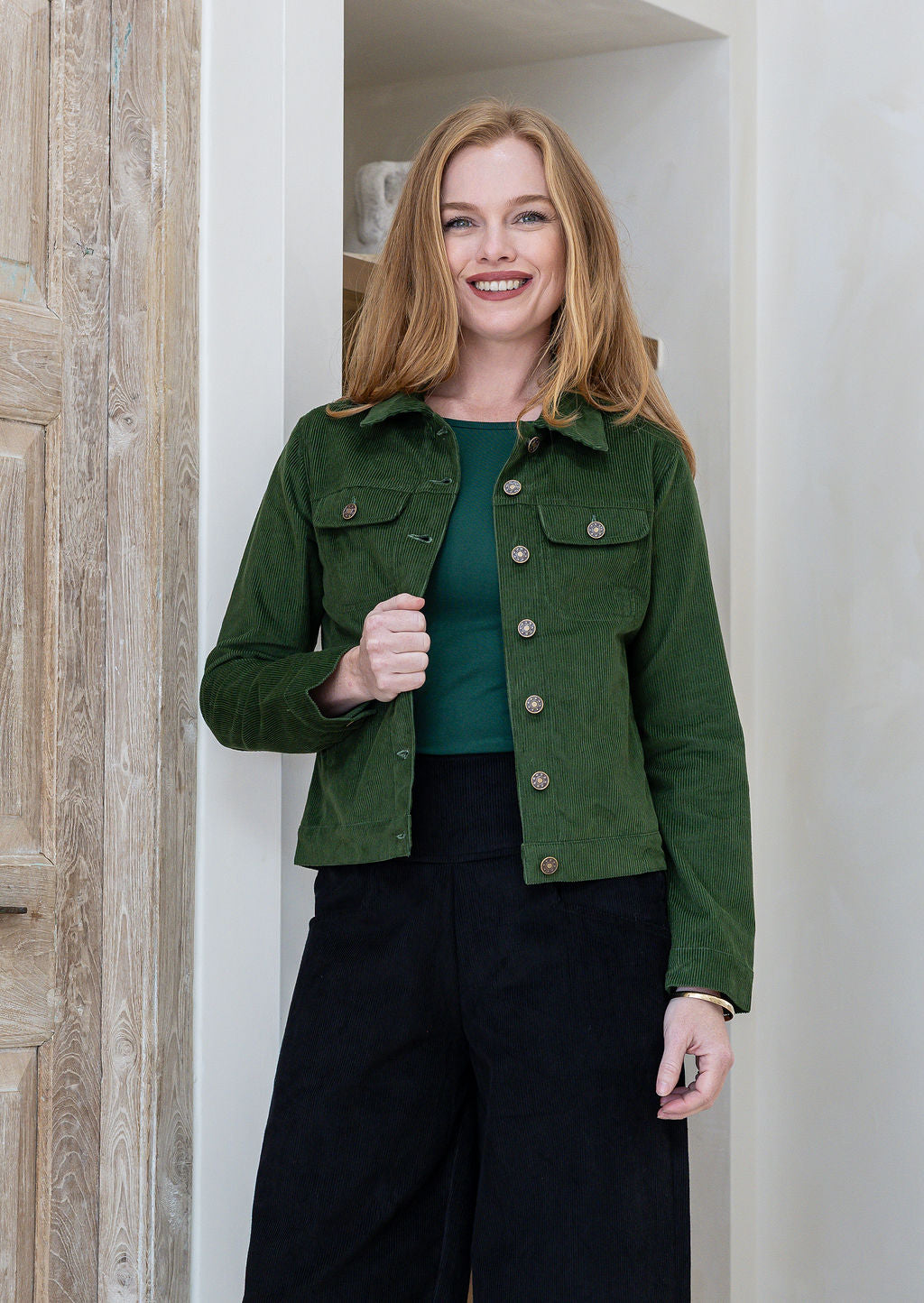 Woman wearing green cotton corduroy jacket with brass buttons paired with plain black pants
