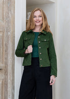 Woman wearing green cotton corduroy jacket with brass buttons paired with plain black pants