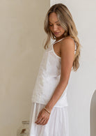 Side view of model wearing white lightweight cotton cami with V-neckline, adjustable spaghetti straps and  picot trim