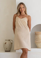 Beige cotton slip for undergarment with thin straps and lace hem, on a model standing against a wall.
