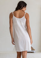 Back view of model wearing white cotton slip undergarment with thin adjustable straps and lace hem, above knee length