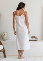 Back view of woman wearing white lightweight cotton maxi slip with adjustable spaghetti straps, side splits and picot trim hem