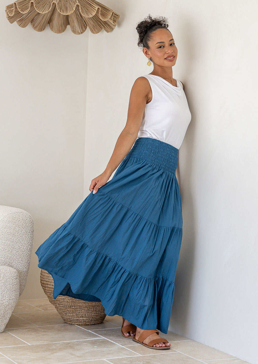 Woman holding out her blue tiered cotton maxi skirt, paired with a white singlet top