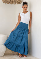 Woman wearing a white top paired with a blue cotton tiered maxi skirt, holding the skirt out to the side