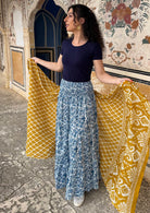 Woman wears a white based blue floral cotton maxi skirt paired with a navy blue stretch t-shirt, holding a yellow shawl around her