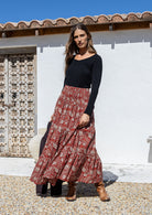 Woman wearing a black top and red floral skirt standing in front of a white wall.