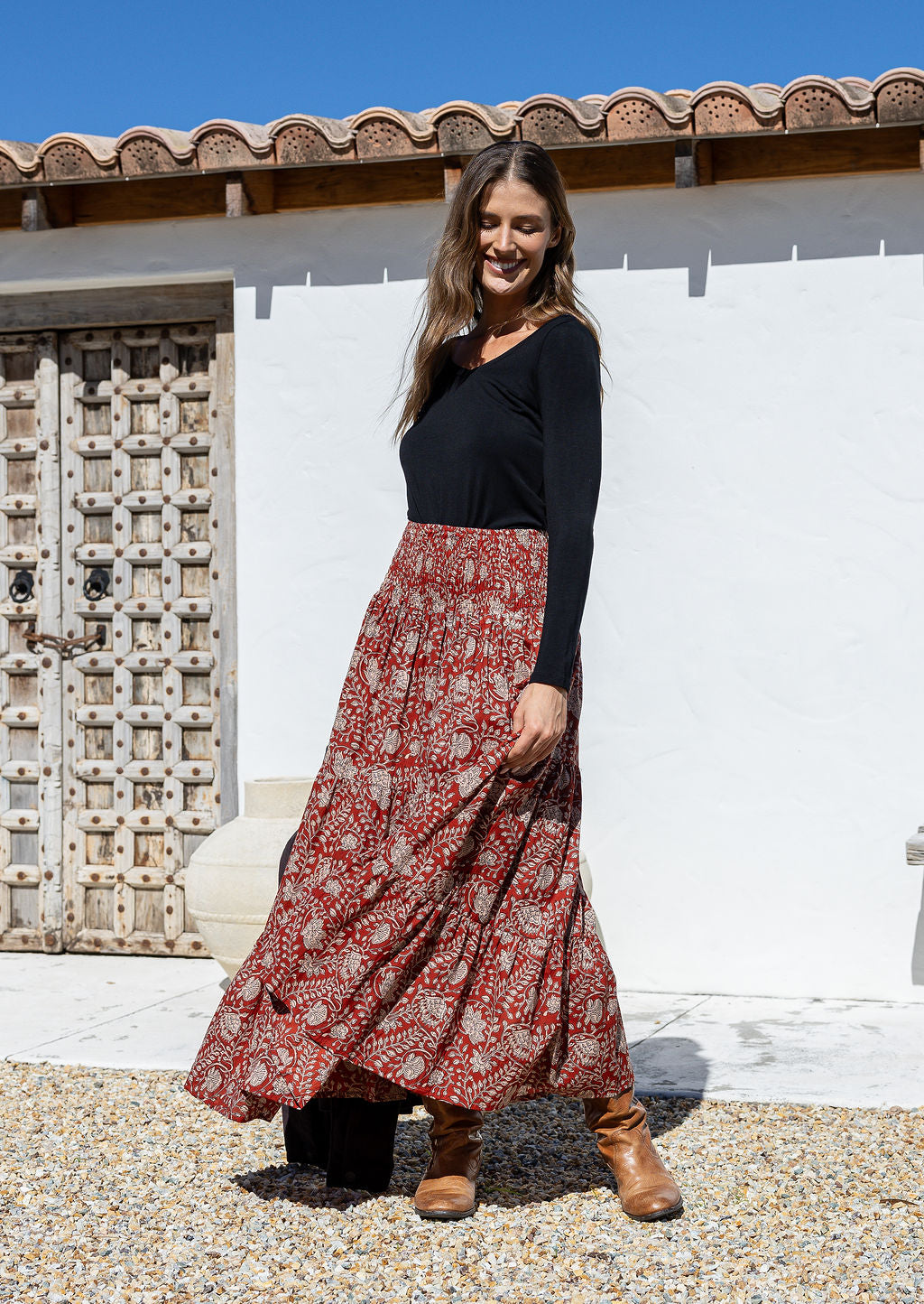 Woman wearing a black top and red patterned skirt standing in front of a white wall and wooden door.