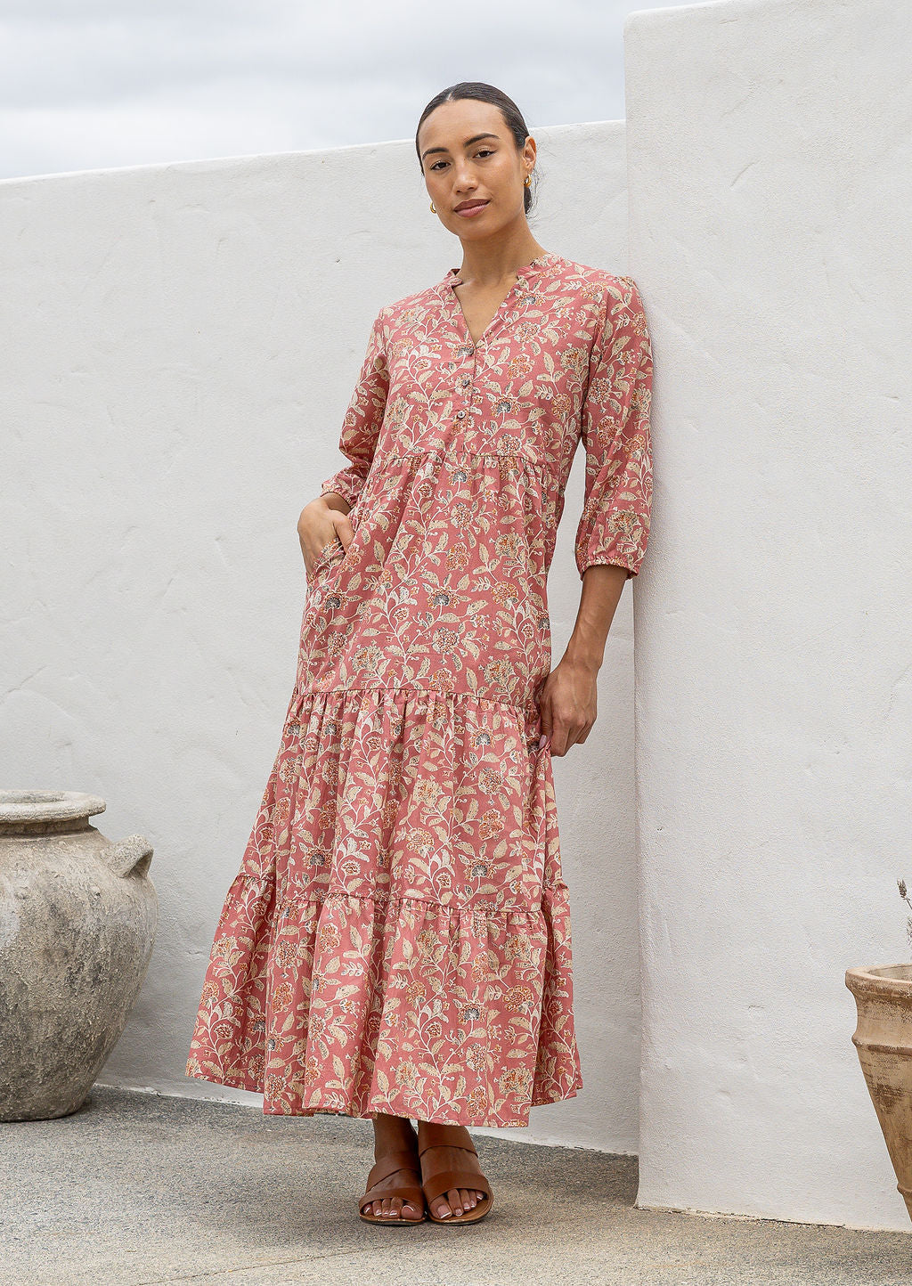 Woman poses in rose pink based floral cotton maxi dress with buttoned bodice, 3/4 sleeves and flowy three tiered maxi skirt