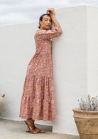 Woman stands side ways wearing a 100% cotton tiered maxi dress in rose pink based floral print with 3/4 sleeves, pockets and mandarin collar