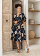 Model posing in over the knee length wrap dress with flowing skirt and formation of V neckline.