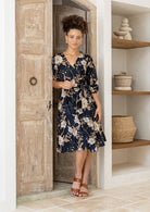 Model wearing 3/4 sleeved black based floral print cotton wrap dress with V-neckline and pockets.