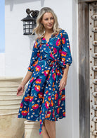 Model posing in over the knee length wrap dress with flowing skirt and formation of V neckline.