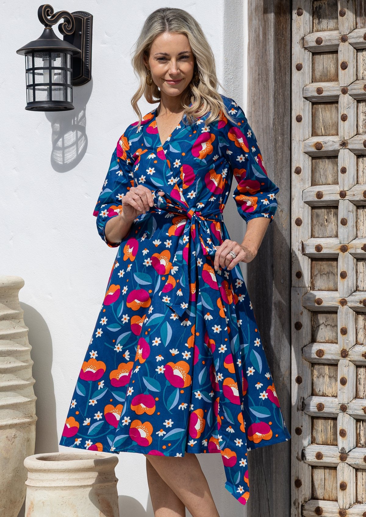 Model wearing 3/4 sleeved royal blue based floral print cotton wrap dress with V-neckline and pockets.