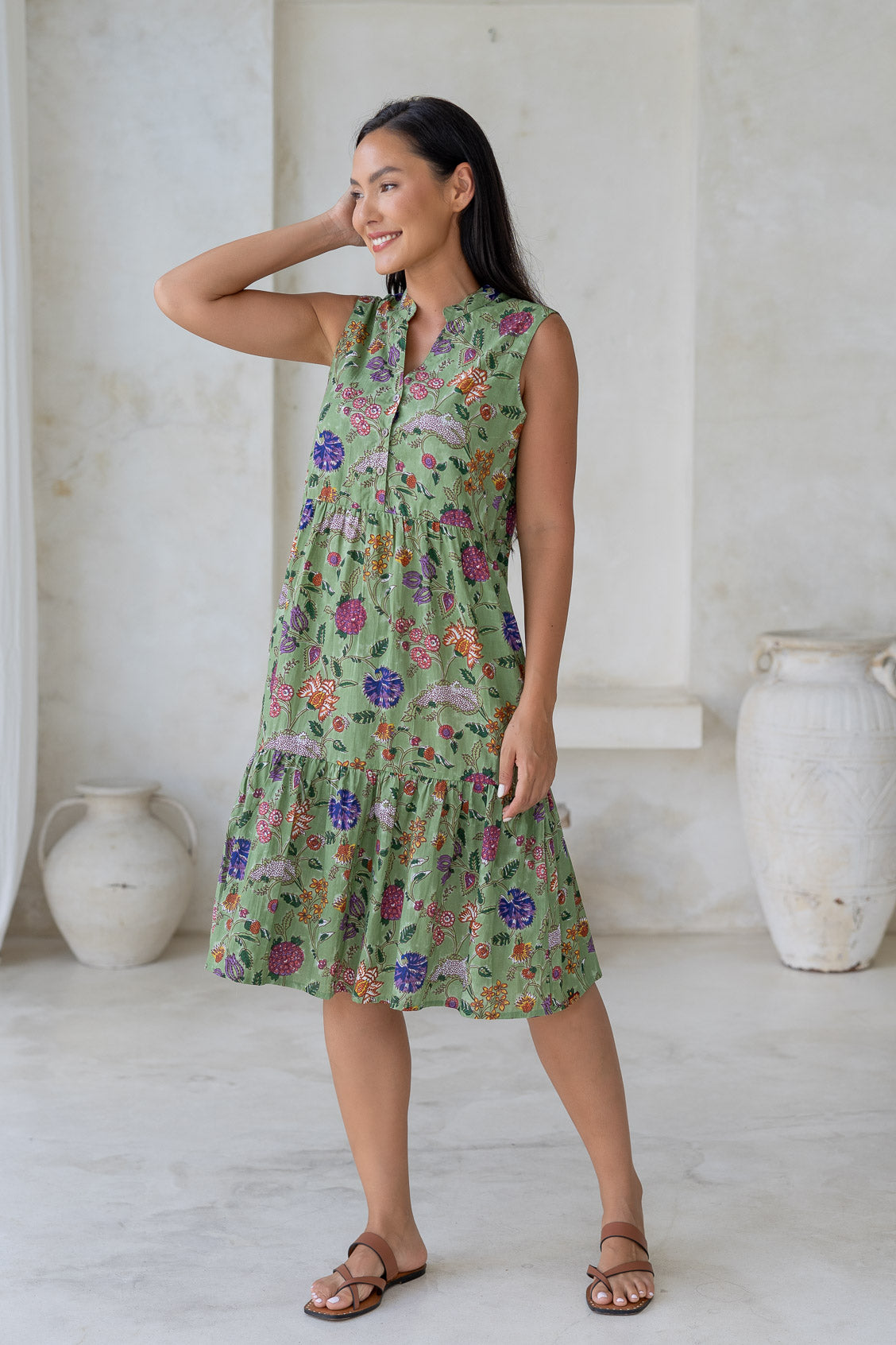 Woman wearing a green floral cotton knee length dress with 2 tiered skirt, buttoned bodice and hidden side pockets.