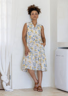 Woman posing in a neutral based floral sleeveless dress with a buttoned bodice, two tiered skirt and mandarin collar 