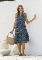 Woman wearing a knee length cotton sleeveless dress with buttoned bodice and  two tiered skirt in navy blue based floral print.