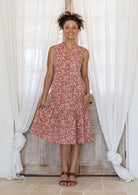 Woman wearing a knee length cotton sleeveless dress with buttoned bodice and  two tiered skirt in rose pink based floral print.