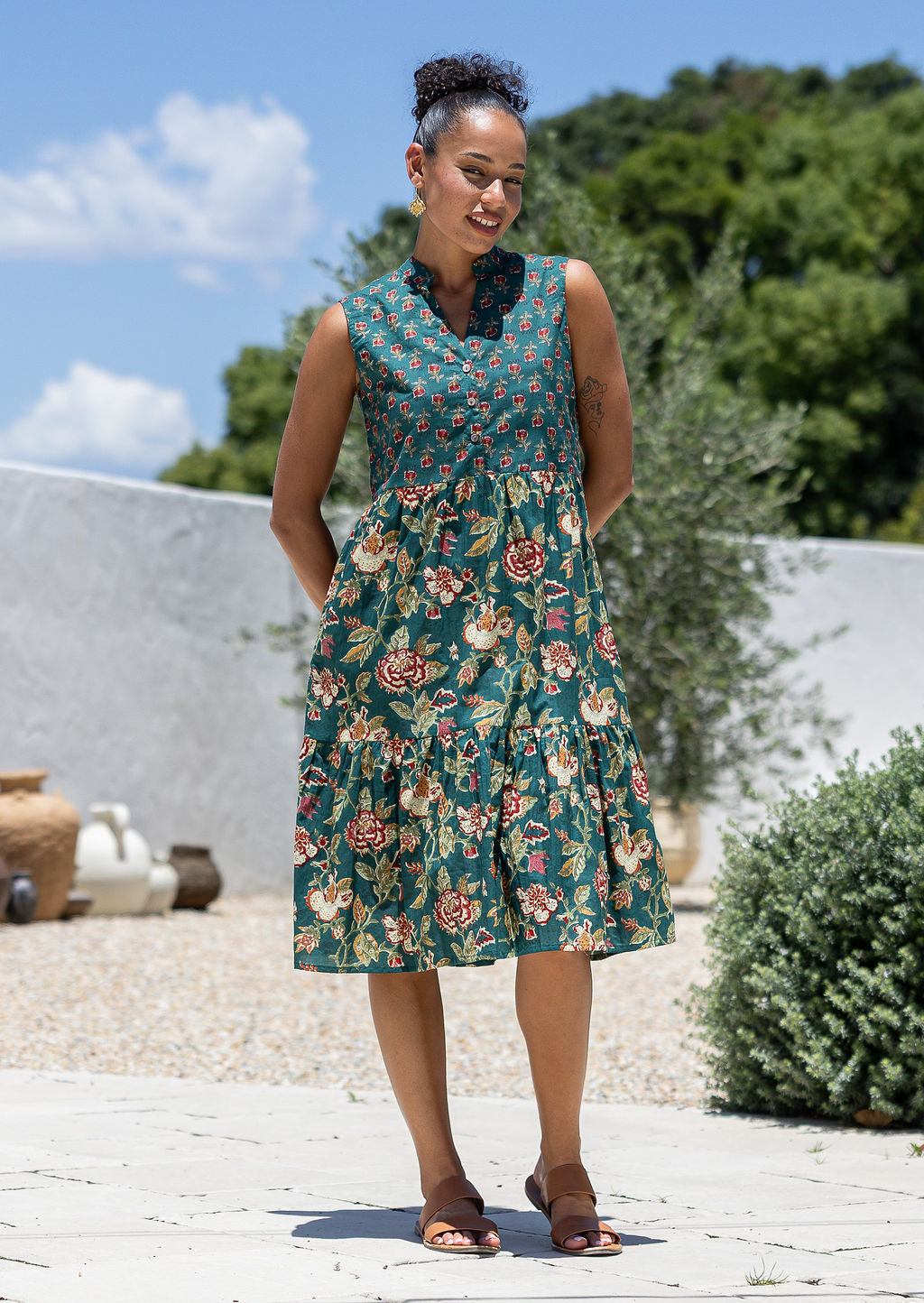 Woman posing in a green based floral sleeveless dress with a buttoned bodice, two tiered skirt and mandarin collar 