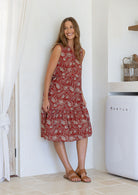 Woman posing in a red based floral sleeveless dress with a buttoned bodice, two tiered skirt and mandarin collar 