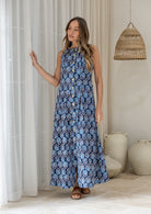 Woman in a navy based floral cotton sleeveless maxi dress standing against white curtains