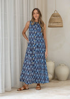 Woman wearing a navy based floral cotton sleeveless button through dress, with high neckline