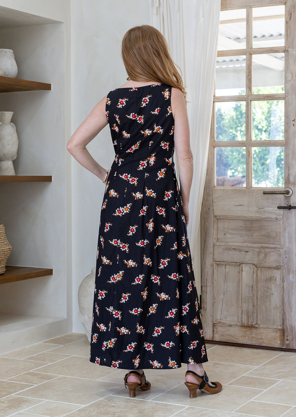 Back view of a woman wearing a sleeveless cotton maxi dress with small floral clusters on a black base