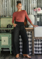 Woman standing in a rustic kitchen wearing black cotton corduroy wide leg pants and a dusty pink top