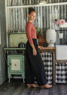 Woman standing side on wearing black cotton corduroy wide leg pants and a dusty pink top